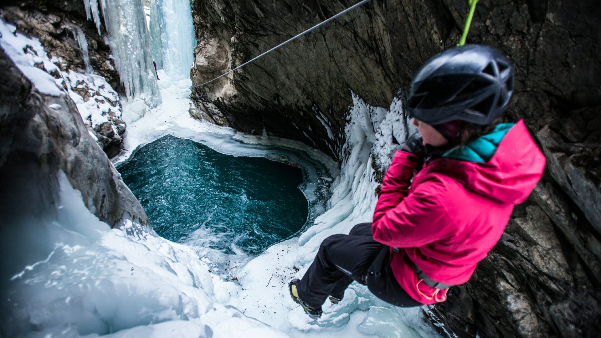 Frozen waterfall, ice cold water pond, woman rappelling